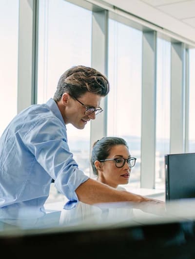 Two coworkers look at dual screens and strategize about future AI projects.